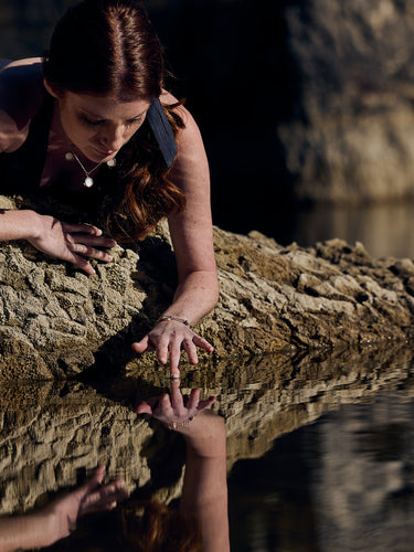 Femme allongé sur un roché touchant l'eau du lac avec ses doigts - Joaillerie éthique
