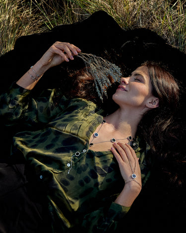 Jeune femme allongée sur le sol dans l'herbe portant un collier et une bague chaine en or Uchéal