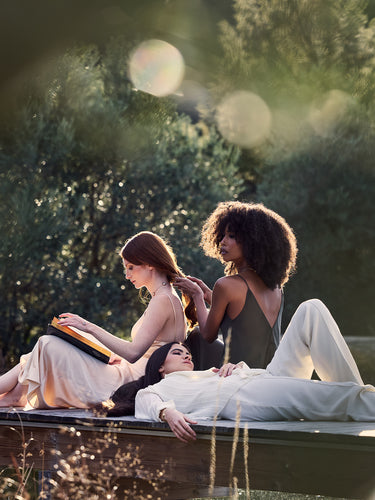 3 jeunes femme installées sur un ponton en train de lire et de se coiffer - haute joaillerie